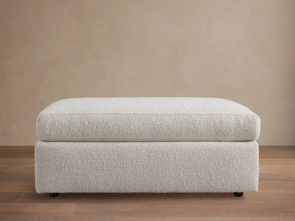 Off-white textured Vernon Square Ottoman, two-part design with plush cushion & sturdy base, on wood floor.
