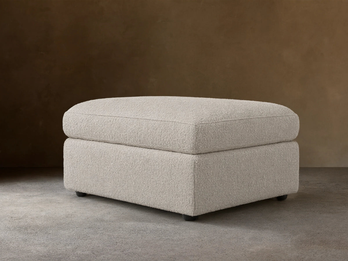 Off-white textured Vernon Square Ottoman, two-part design with plush cushion & sturdy base, on wood floor.