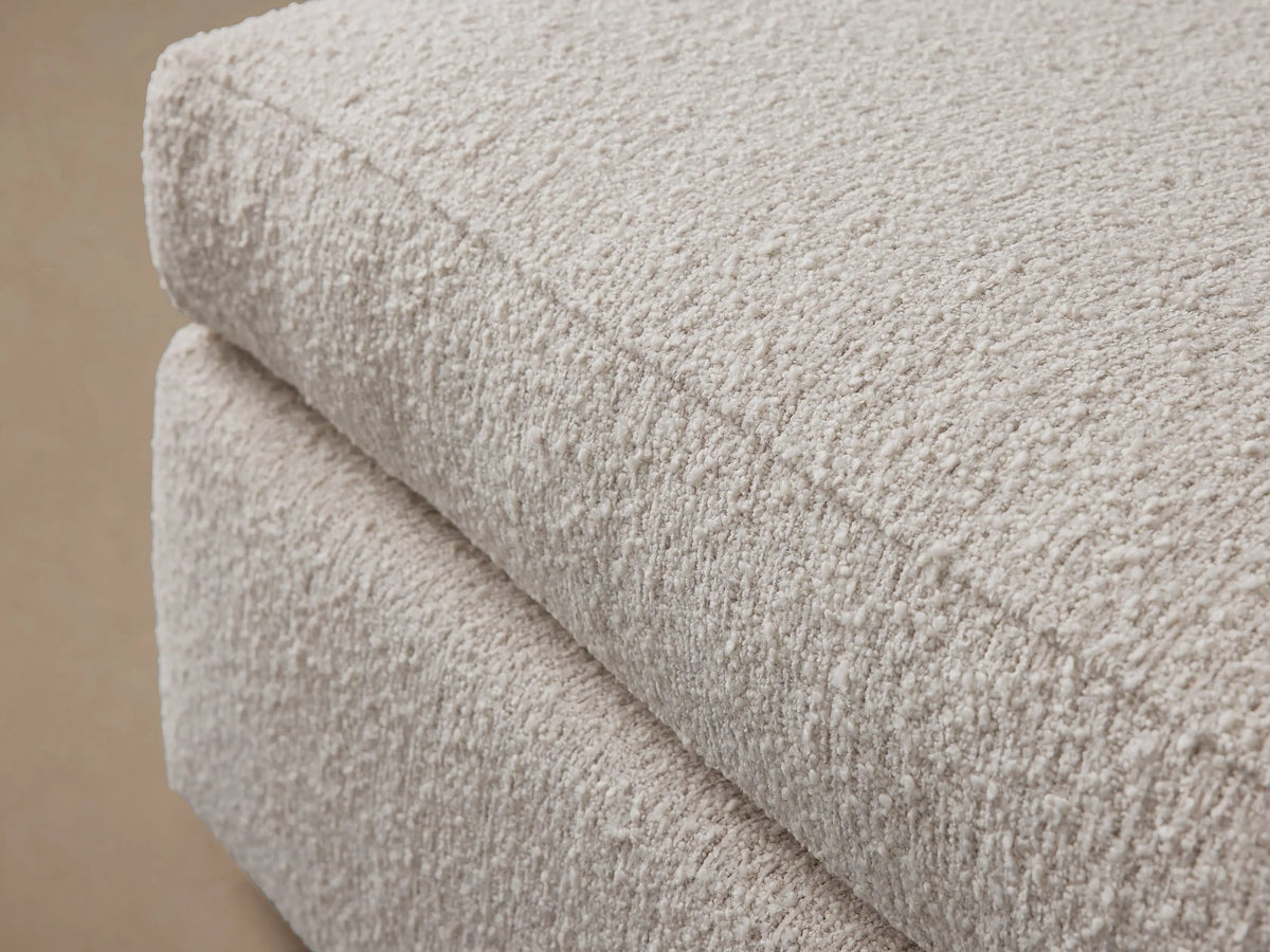 Off-white textured Vernon Square Ottoman, two-part design with plush cushion & sturdy base, on wood floor.