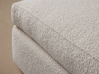 Off-white textured Vernon Square Ottoman, two-part design with plush cushion & sturdy base, on wood floor.