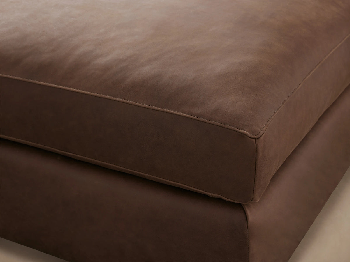 Vernon Leather Ottoman in rich brown leather, showcasing a smooth, cushioned top and precise stitching along the edges.