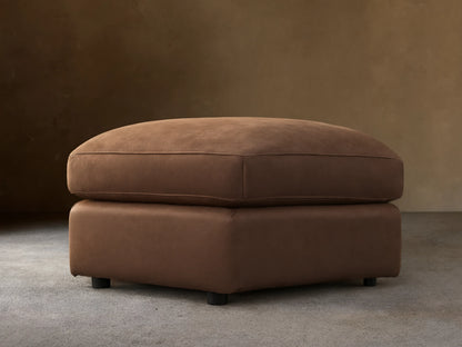 Vernon Leather Ottoman in rich brown leather, rectangular shape, flat top cushion, and low legs, set on wooden floor.