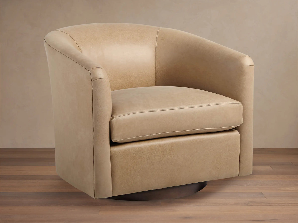 Light beige leather Bowan Swivel Chair, barrel-shaped with rounded arms and dark circular swivel base on a wood floor.