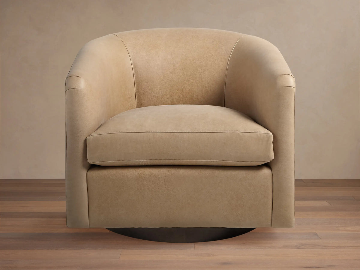 Light beige leather Bowan Swivel Chair, barrel-shaped with rounded arms and dark circular swivel base on a wood floor.