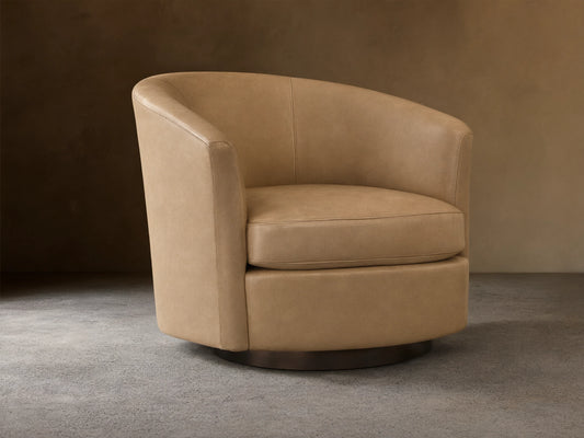 Light beige leather Bowan Swivel Chair, barrel-shaped with rounded arms and dark circular swivel base on a wood floor.