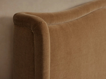 Winslet Bed, full view, with a tall, curved, winged camel-colored upholstered headboard & frame, dressed with white bedding.