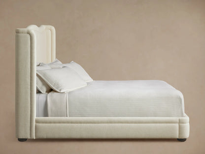 Close-up of the Winslet Bed's curved headboard corner, showing textured cream-colored upholstery fabric against a beige wall.