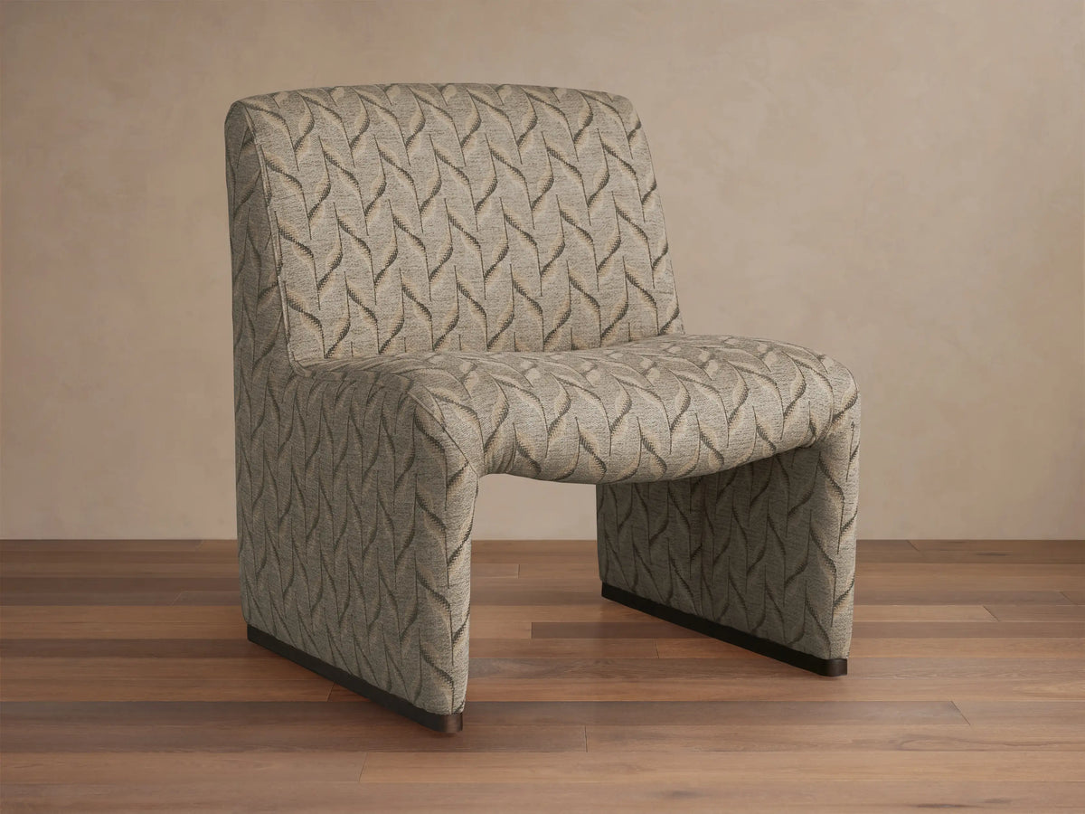 Reyna Chair, armless slipper chair with beige and dark grey leaf pattern fabric, angled on a hardwood floor.