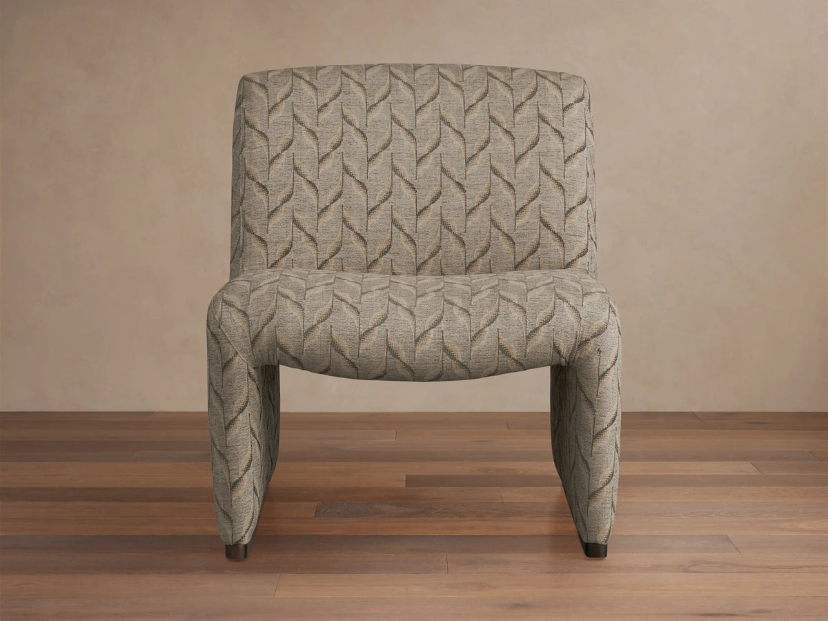 Reyna Chair, armless slipper chair with beige and dark grey leaf pattern fabric, angled on a hardwood floor.