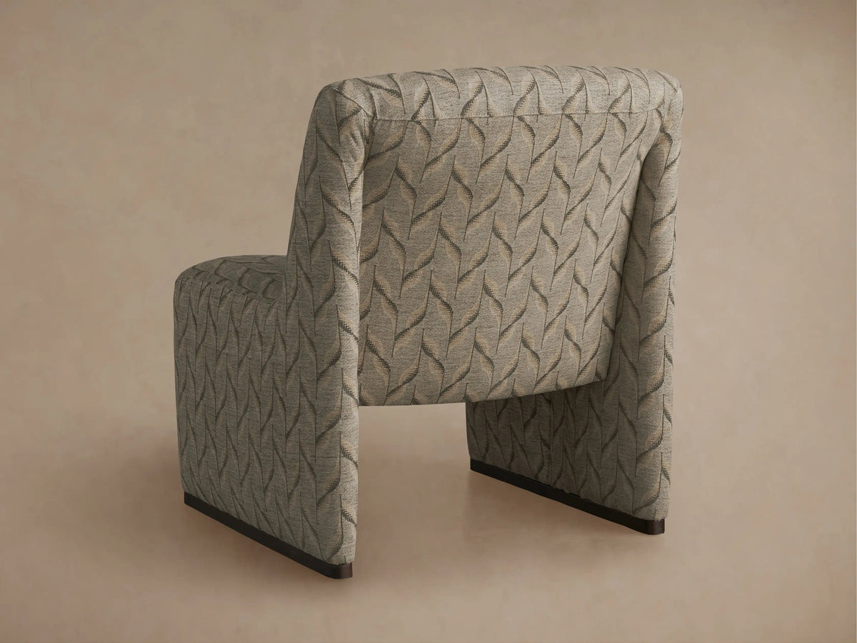 Close-up, angled view of Reyna Chair's back, light grey textured fabric with dark grey and light brown wavy leaf-like pattern.