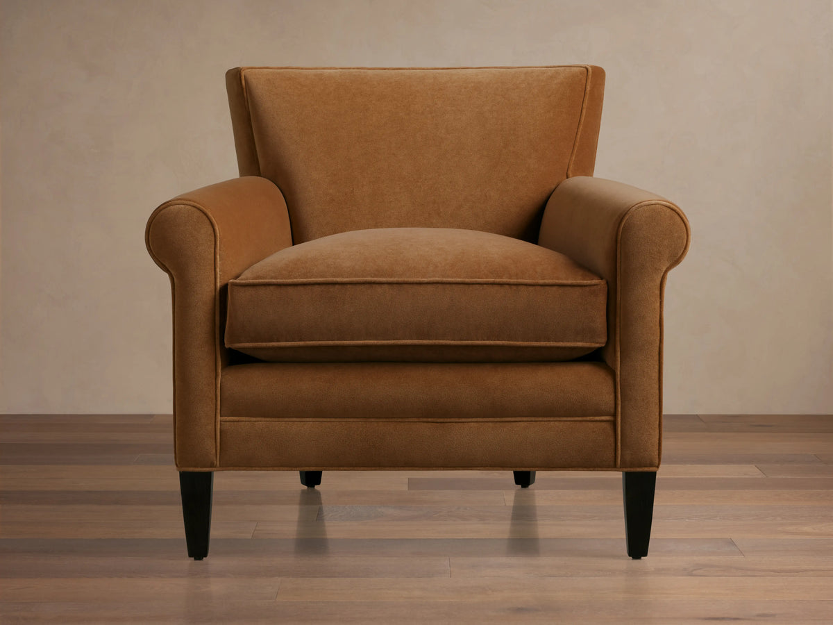 Back view of a Rudy Rolled Arm Chair showcasing its cognac velvet upholstery, rolled arms, and dark tapered wooden legs on a light background.