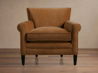 Back view of a Rudy Rolled Arm Chair showcasing its cognac velvet upholstery, rolled arms, and dark tapered wooden legs on a light background.