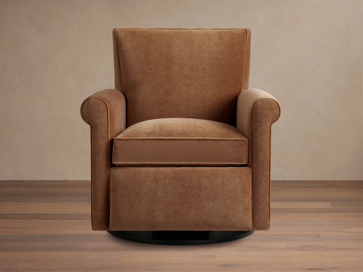 Rudy Rolled Arm Swivel Recliner in cognac velvet, featuring a high back, plush seat cushion, and rounded arms on a wooden floor.