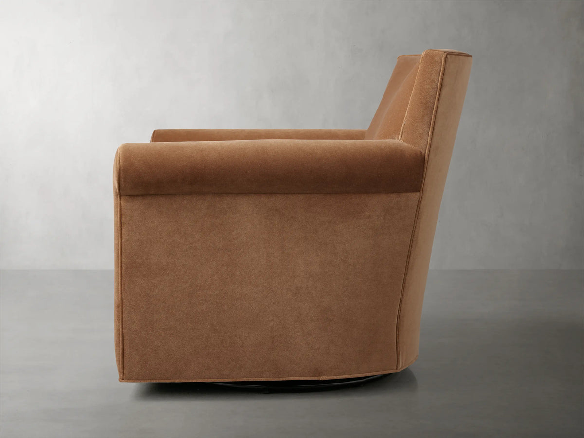 Rudy Rolled Arm Swivel Chair in Banks Cognac, rear view; cognac velvet fabric, rounded back, on a gray floor.