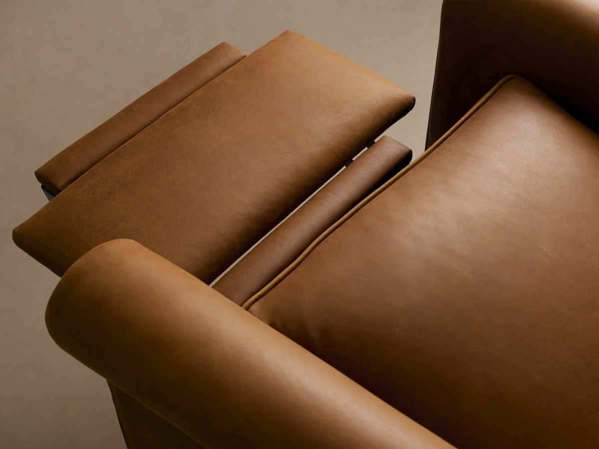 Rudy Leather Rolled Arm Swivel Recliner in brown leather, features rolled arms, a cushioned backrest, and 360-degree swivel base on wooden floor.