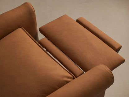 Close-up of Rudy Leather Rolled Arm Swivel Recliner. Warm brown leather, showing the distinct rolled arm, cushioned seat, and fine piping.