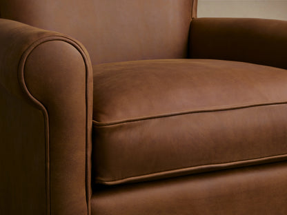Rudy Leather Rolled Arm Swivel Chair in brown leather, featuring rolled arms and a cushioned seat on a wooden floor.