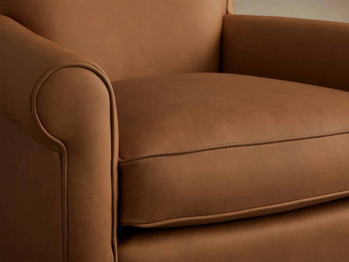 Rudy Leather Rolled Arm Swivel Chair, a luxurious tan leather chair with rolled arms and a plush seat, centered on a wood floor.