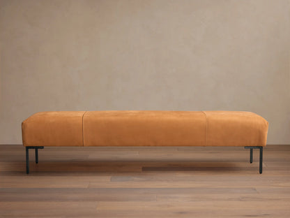 Tilton Leather Bench, long caramel leather bench with rounded ends, two seams, and black metal legs on a wood floor.