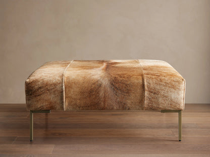 Tilton Hair on Hide Ottoman, rectangular, upholstered in blonde brindle hair-on-hide with gold metal legs, on wood floor.