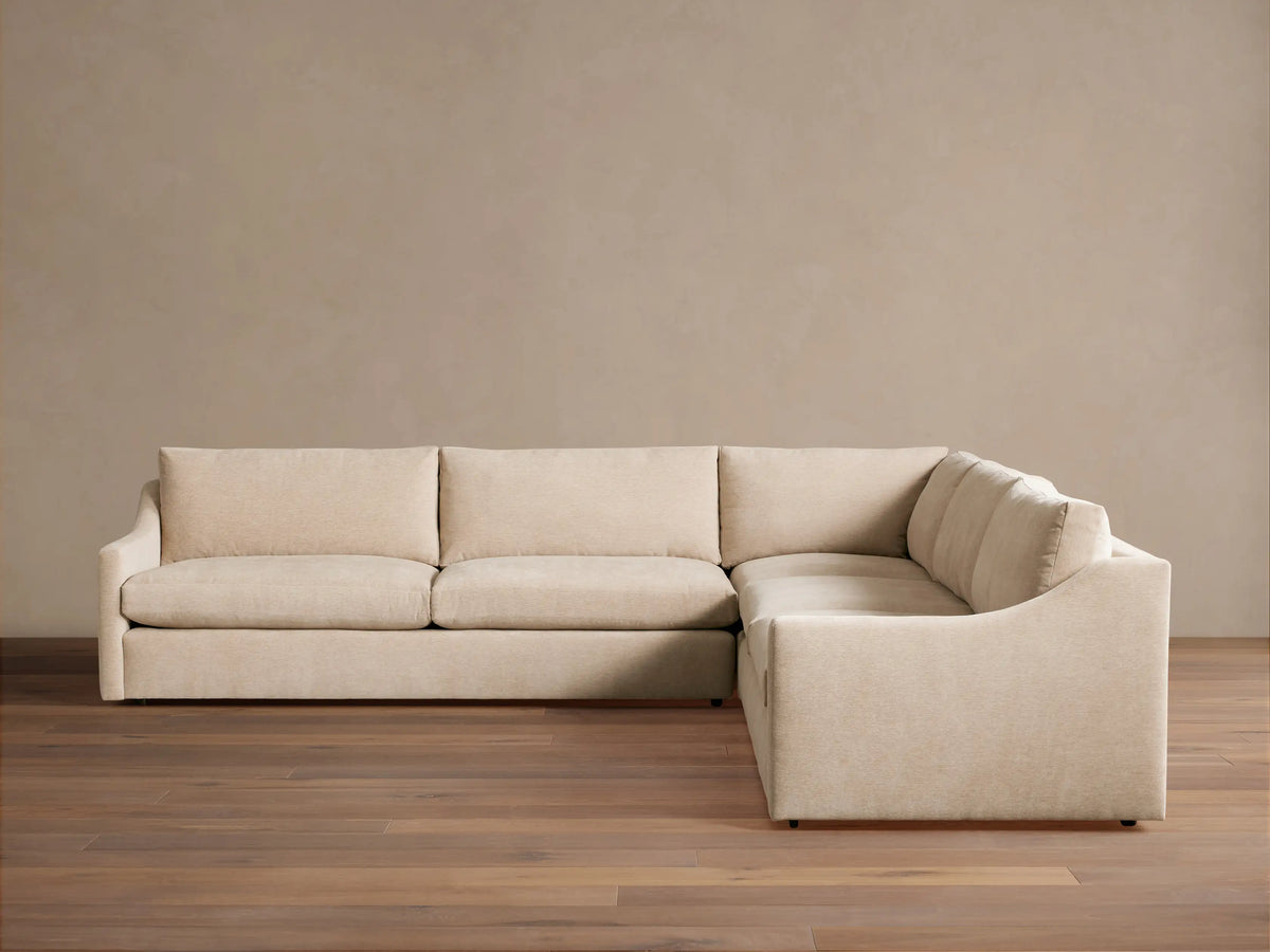 Kipton Slope Arm Three-Piece Corner Sectional in light beige fabric, L-shaped with subtly sloped arms, on a wood floor.
