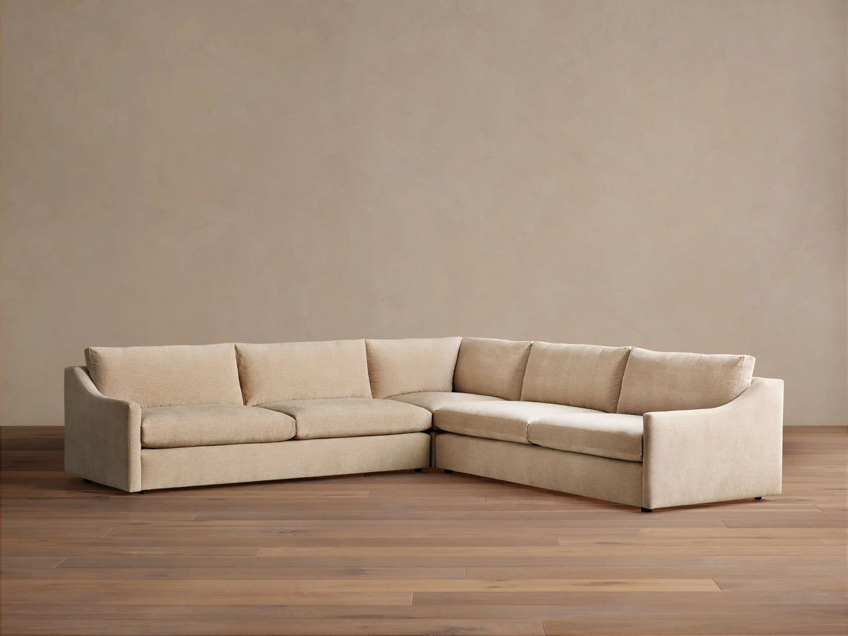 Kipton Slope Arm Three-Piece Corner Sectional in light beige fabric, L-shaped with subtly sloped arms, on a wood floor.