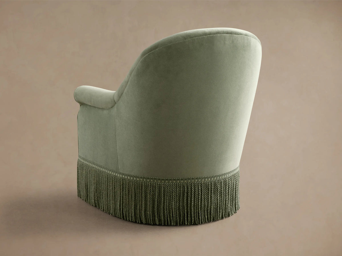 Front view of the sage green Augustus Swivel Chair with Fringe, featuring a curved back, rolled arms, and long fringe.
