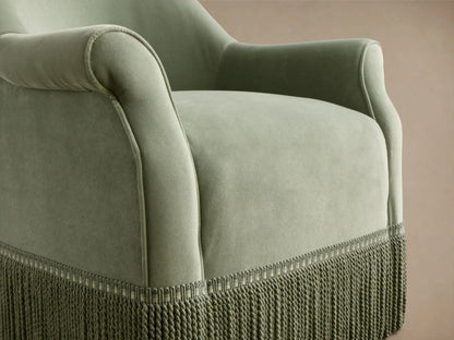 Rear-side view of the sage green Augustus Swivel Chair with Fringe, with a rolled arm and full fringe detail at the base.