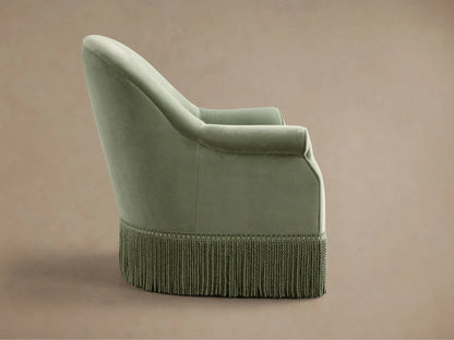 Close-up, angled view of a sage green Augustus Swivel Chair with Fringe, highlighting the rolled armrest and braided fringe.
