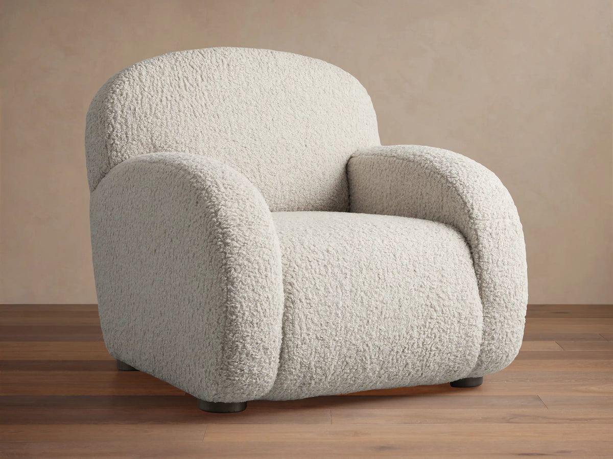 Algiers Chair, light cream bouclv© textured armchair with rounded back and arms, angled left on a wooden floor.