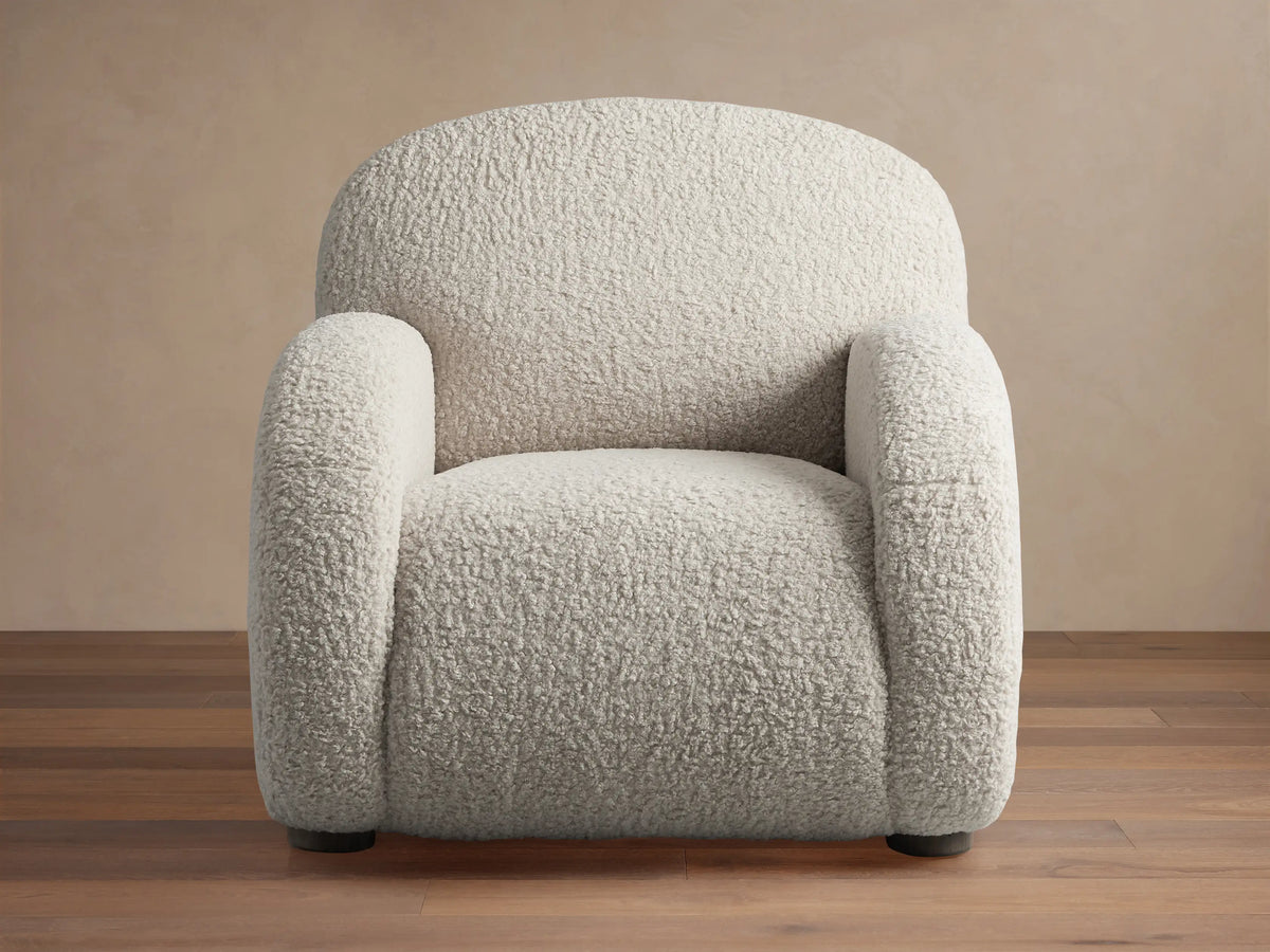 Algiers Chair, a plush off-white textured armchair with rounded arms and back, shown on a wooden floor.