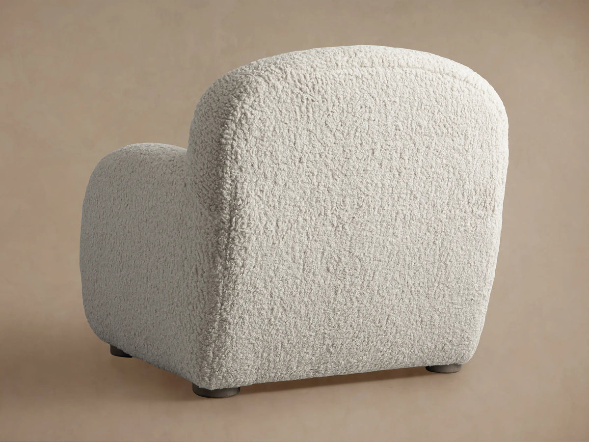 Algiers Chair, a rounded armchair with a soft, off-white bouclv© fabric upholstery, seen from the back on a neutral background.