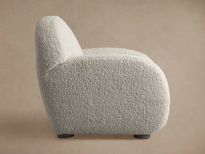 Light gray shaggy Algiers Chair, side view, with rounded contours and dark low-profile feet, against a beige background.