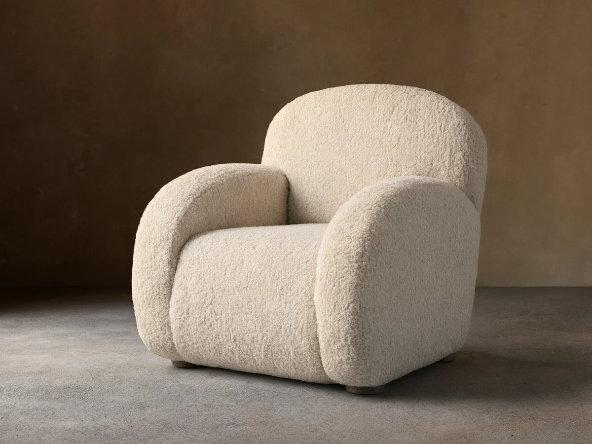 Algiers Chair, light cream bouclv© textured armchair with rounded back and arms, angled left on a wooden floor.