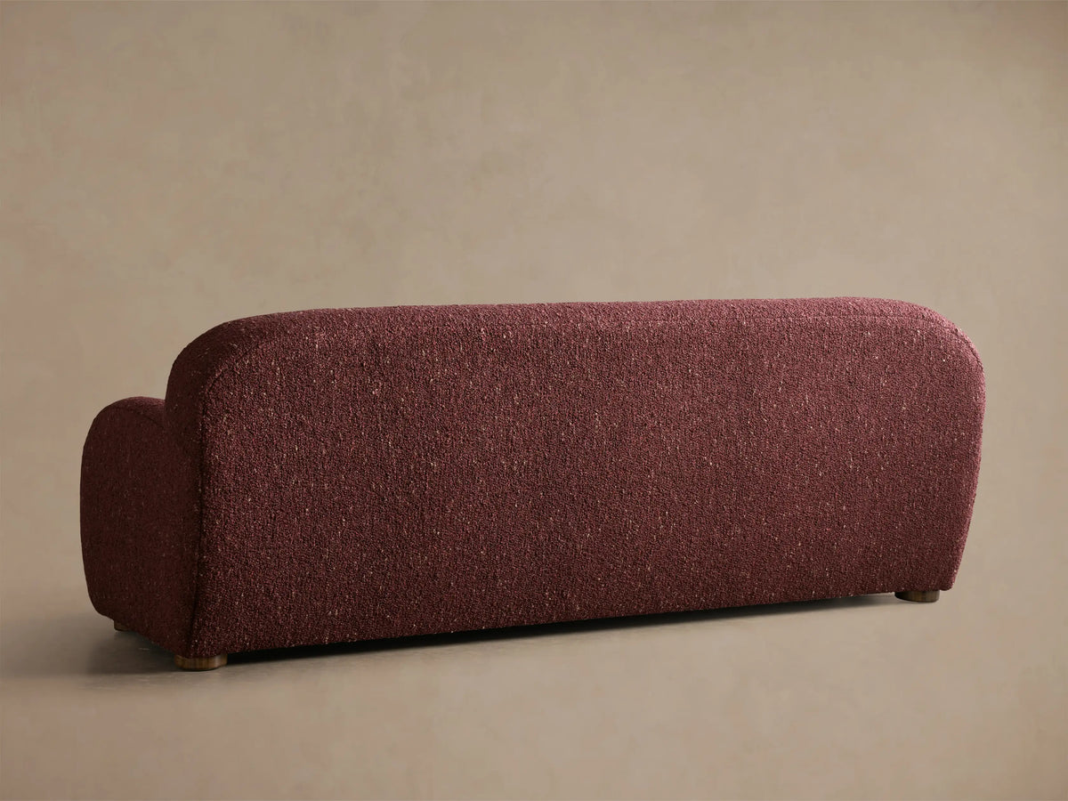Close-up of the burgundy Algiers Sofa, showing its curved armrest and textured, nubbly bouclé fabric.