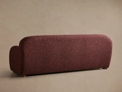 Close-up of the burgundy Algiers Sofa, showing its curved armrest and textured, nubbly bouclé fabric.
