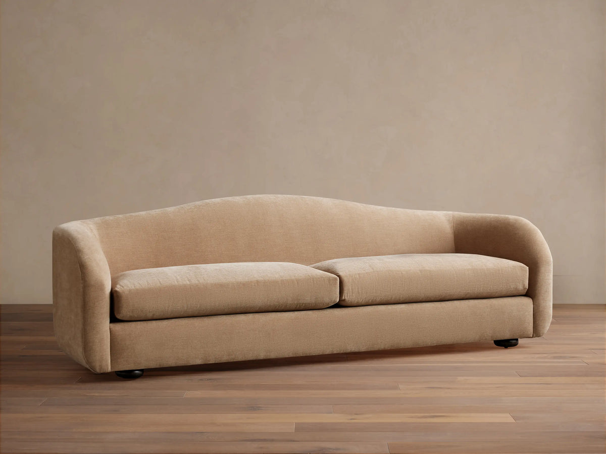 Ashlyn two-seat sofa with a curved back and integrated arms, upholstered in a light tan textured fabric.