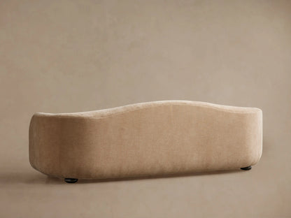 Angled close-up of the Ashlyn Two-Seat Sofa. Shows the soft, textured beige fabric and a gracefully curved arm and backrest.