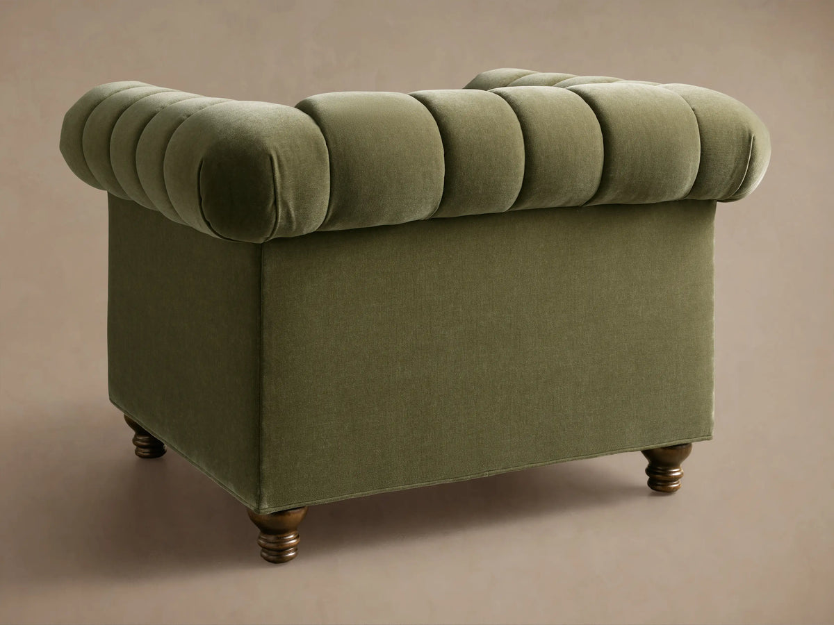 Close-up of olive green Berwick Channeled Chair, velvet upholstery with rolled arms, channeled back and seat cushions, dark wood legs.