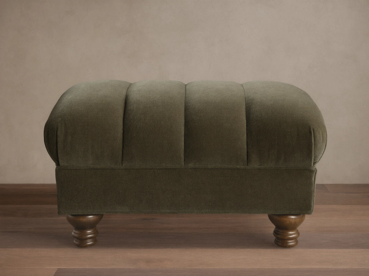 Front view of the olive green Berwick Channeled Ottoman, featuring channel-stitched detailing on its upholstered top and turned wood feet.