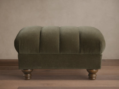 Front view of the olive green Berwick Channeled Ottoman, featuring channel-stitched detailing on its upholstered top and turned wood feet.