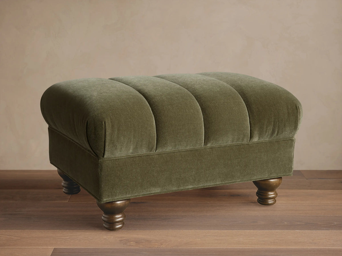 Front view of the olive green Berwick Channeled Ottoman, featuring channel-stitched detailing on its upholstered top and turned wood feet.