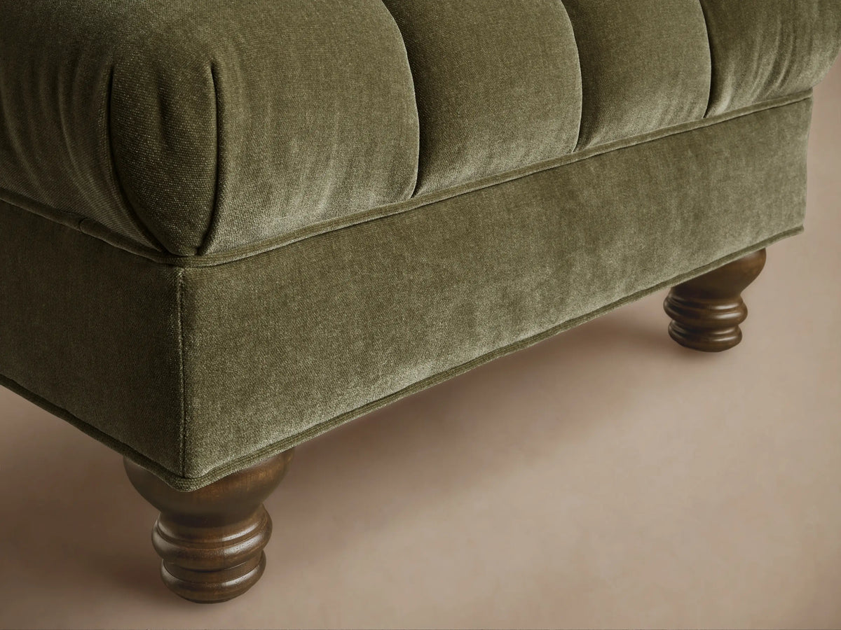 Front view of the Olive Berwick Channeled Ottoman, featuring a channeled velvet top and dark turned wooden legs.