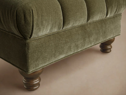 Front view of the Olive Berwick Channeled Ottoman, featuring a channeled velvet top and dark turned wooden legs.