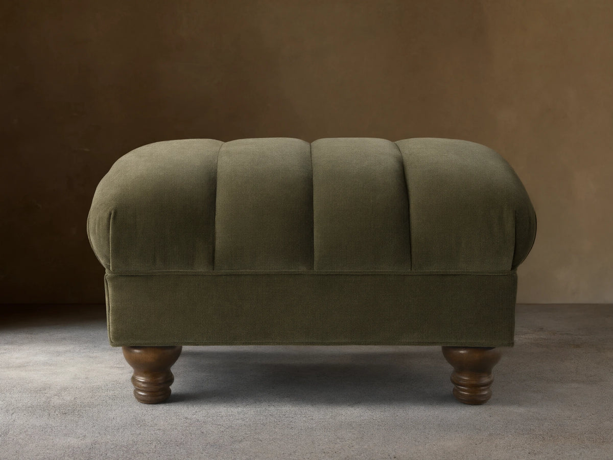 Front view of the olive green Berwick Channeled Ottoman, featuring channel-stitched detailing on its upholstered top and turned wood feet.