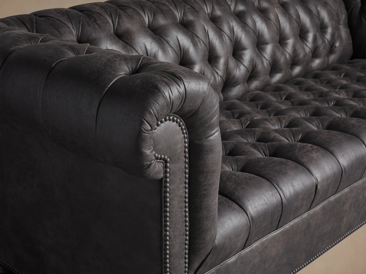 Berwick Faux Leather Sofa, Norre Steel, with deep tufting, rolled arms, nailhead trim, and turned dark legs on a wood floor.