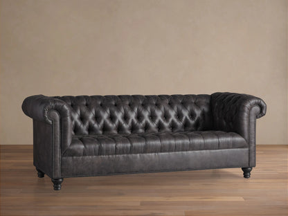 Berwick Faux Leather Sofa in Norre Steel, deeply tufted with rolled arms and nailhead trim, on a wood floor.