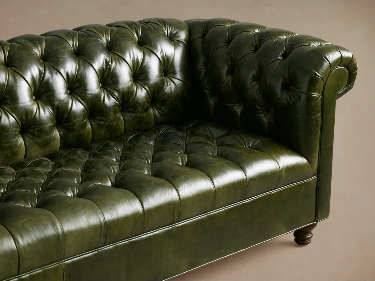 Full view of a dark green Berwick Leather Sofa with tufted back & rolled arms, dark walnut turned legs, on a wooden floor.