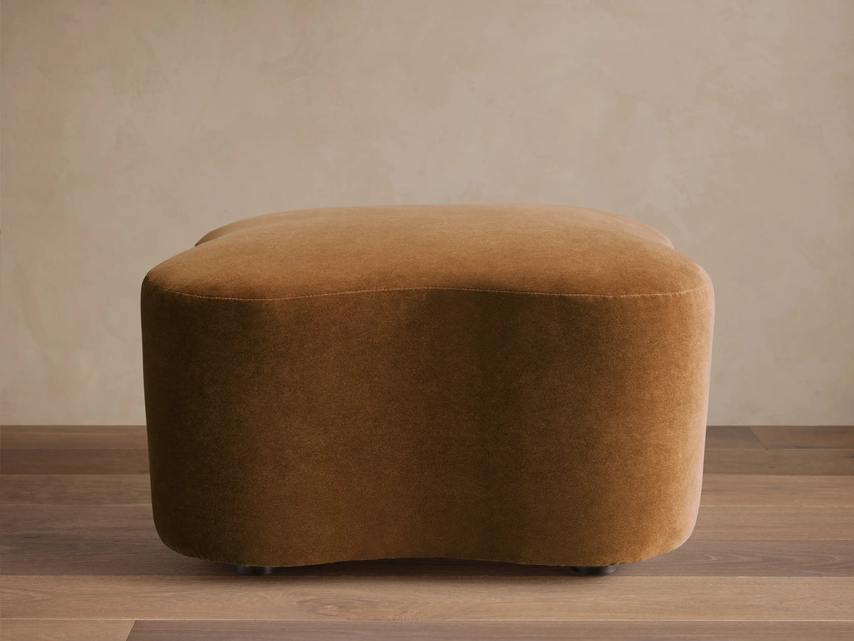 Front view of a brown velvet upholstered Barbey Ottoman with a rounded, organic shape.