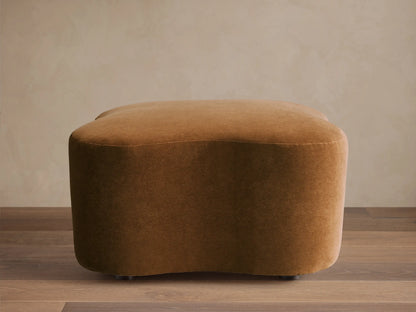 Front view of a brown velvet upholstered Barbey Ottoman with a rounded, organic shape.